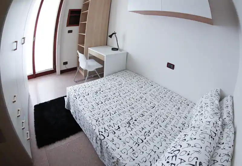 Bright, modern single bedroom with a patterned double bed, built-in wardrobe, small desk and natural light from a balcony door — ideal for a student or professional.