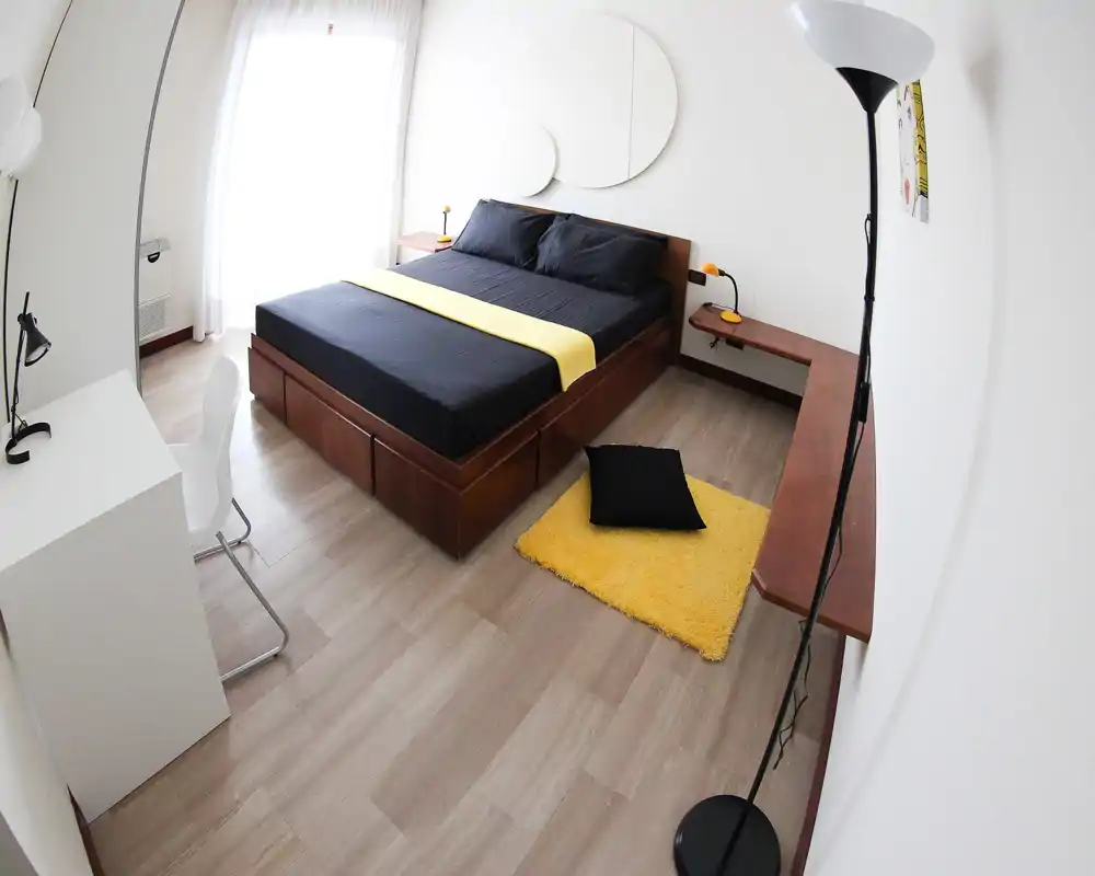Dormitorio moderno y luminoso con cama plataforma de madera vestida en negro y una banda amarilla, alfombra amarilla acogedora y zona de escritorio sencilla — muy iluminado y atractivo para anuncios.