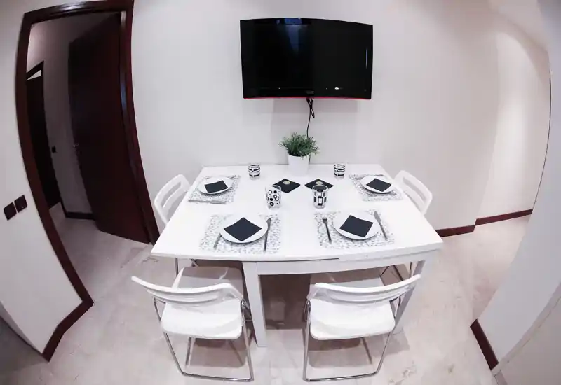 Bright, modern dining area with a set table for four, minimalist white furniture and a small plant centerpiece.