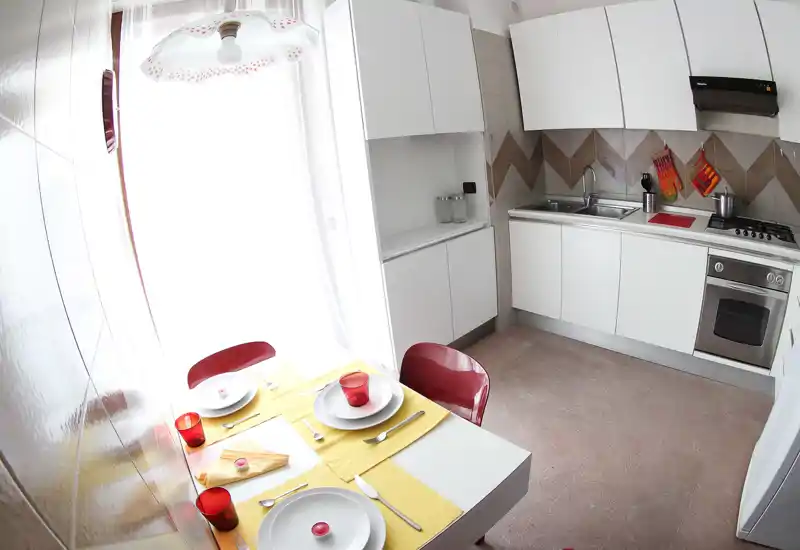 Bright, compact kitchen with white cabinetry, built-in oven and a small dining table set for three — modern and efficiently arranged for short stays.