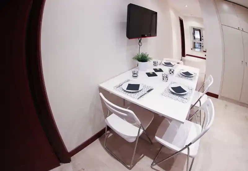 Bright modern dining corner with a white table set for four; clean minimalist styling, placemats and a small plant create a tidy, welcoming atmosphere.