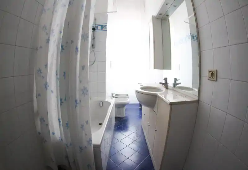 Baño compacto y luminoso con bañera y cortina de ducha, lavabo con encimera y espejo, y inodoro al fondo.