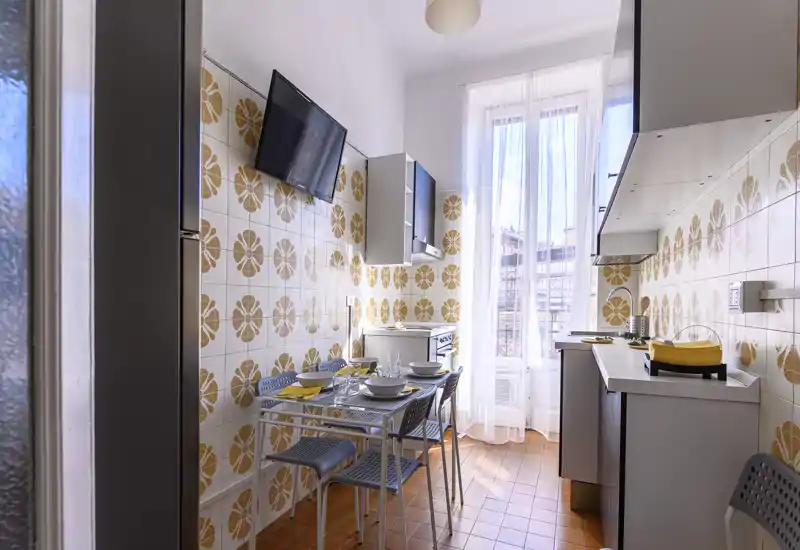 Bright, retro-style kitchen with patterned tile walls, a small dining table set for four, modern cabinetry and a tall window providing abundant natural light.