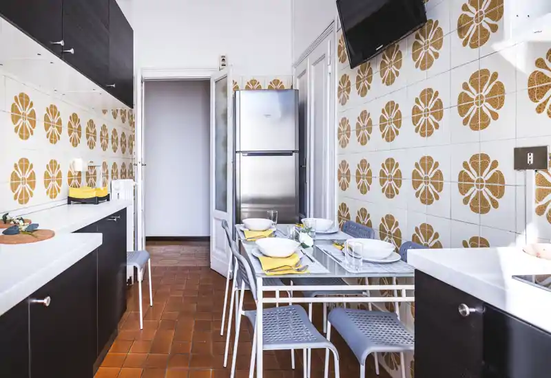 Bright, well-arranged kitchen with a small dining table set for four, modern dark cabinets and decorative tiled walls creating a cheerful retro look.