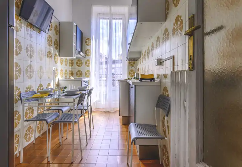Bright, retro-styled galley kitchen with patterned tiles, a small dining table set for four, and a large window providing natural light.