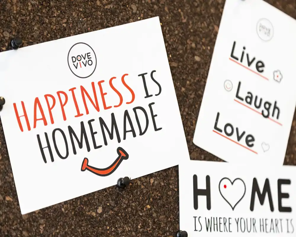 Primo piano di cartoline decorative appuntate su una bacheca di sughero con messaggi positivi e grafiche semplici; dettaglio d'arredo, non la vista di una stanza.