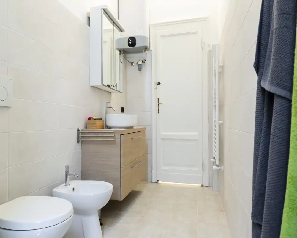 Bagno luminoso e moderno con mobile lavabo sospeso, lavabo a ciotola, bidet e WC; piastrelle neutre e asciugamani rendono l'ambiente pulito e contemporaneo.