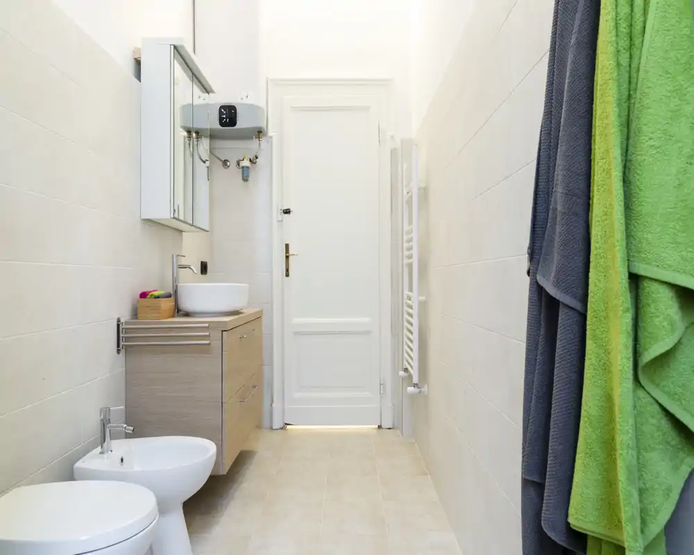 Bagno moderno e luminoso con mobile sospeso, lavabo a ciotola, bidet e WC; piastrelle chiare e scalda salviette che donano un aspetto pulito e minimale.