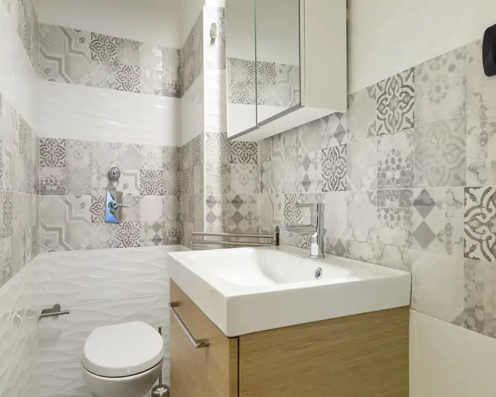 Bagno moderno e luminoso con piastrelle decorative, mobile lavabo compatto con specchio a muro e wc sospeso — perfetto per un appartamento di piccole dimensioni.