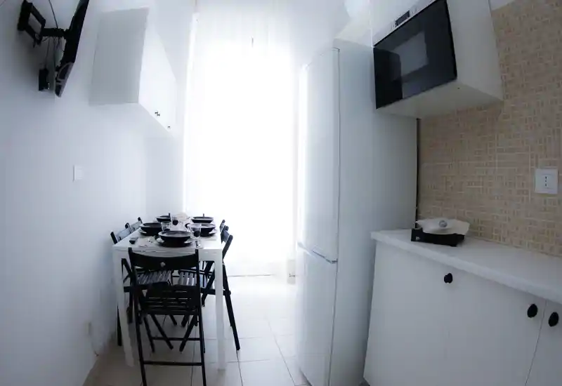 Cuisine compacte et lumineuse avec une table dressée pour quatre, placards blancs, crédence carrelée et électroménagers encastrés — style moderne et minimaliste.