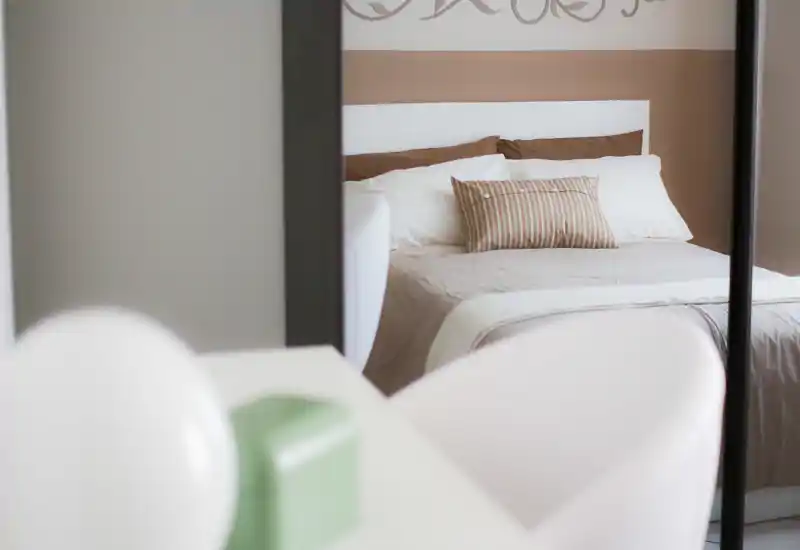 Camera da letto luminosa e dallo stile caldo con letto matrimoniale ben visibile, cuscino decorativo a righe e biancheria neutra e morbida — ambiente accogliente.