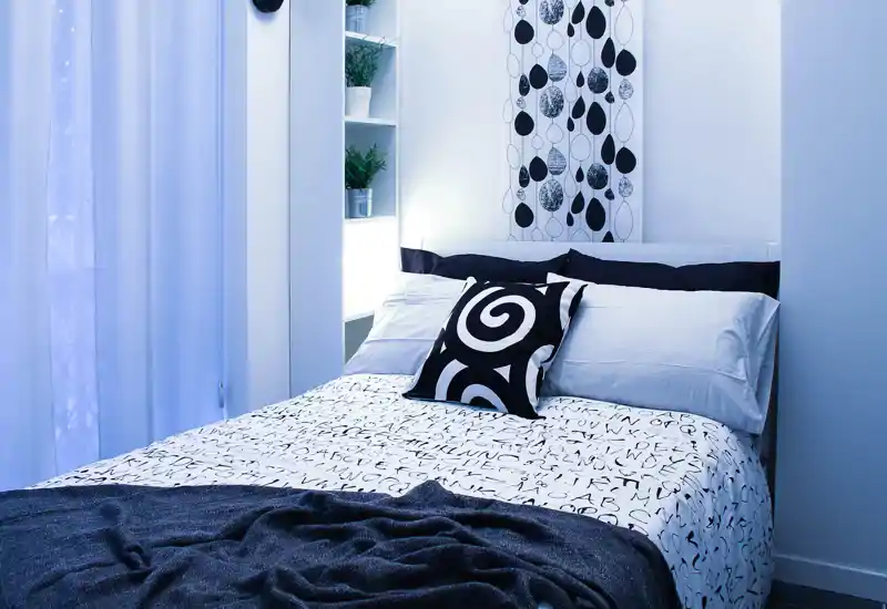 Bright, modern bedroom with a neatly made double bed, patterned cushions and minimal, stylish decor creating a calm, welcoming atmosphere.