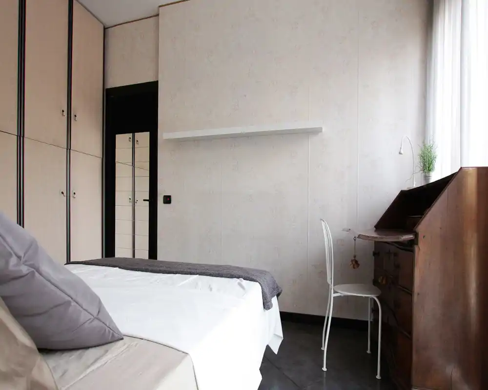 Bright, well-styled bedroom with a large bed, soft textiles and a wooden writing desk by the window. Neutral tones and natural light create a calm, comfortable atmosphere ideal for restful stays.