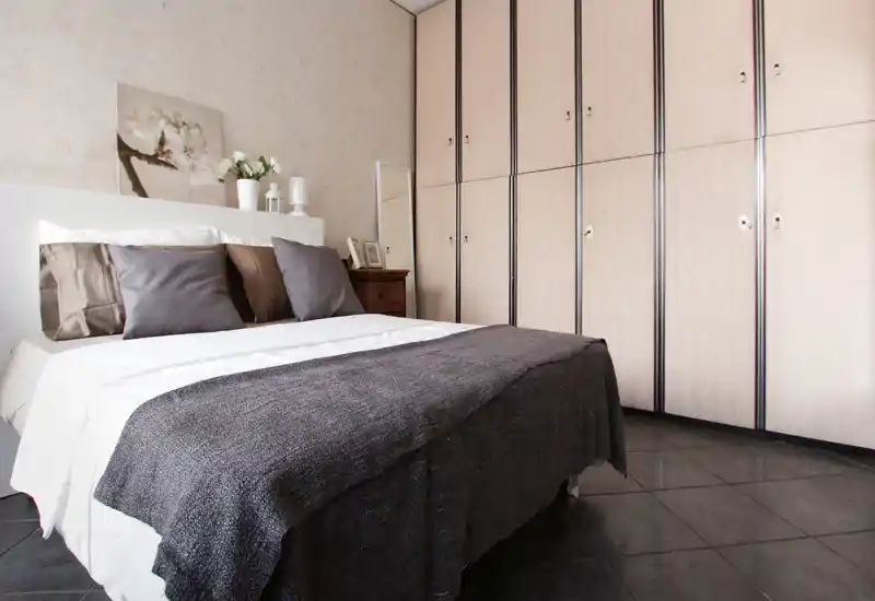 Bright, well-styled bedroom with a double bed dressed in neutral linens, decorative cushions and a large built-in wardrobe along the wall.