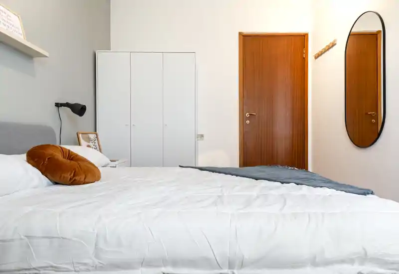 Bright, modern bedroom with a large made bed, accent pillow and simple wardrobe. The clean linens, soft headboard and warm decorative tones create a welcoming space ideal for listings.