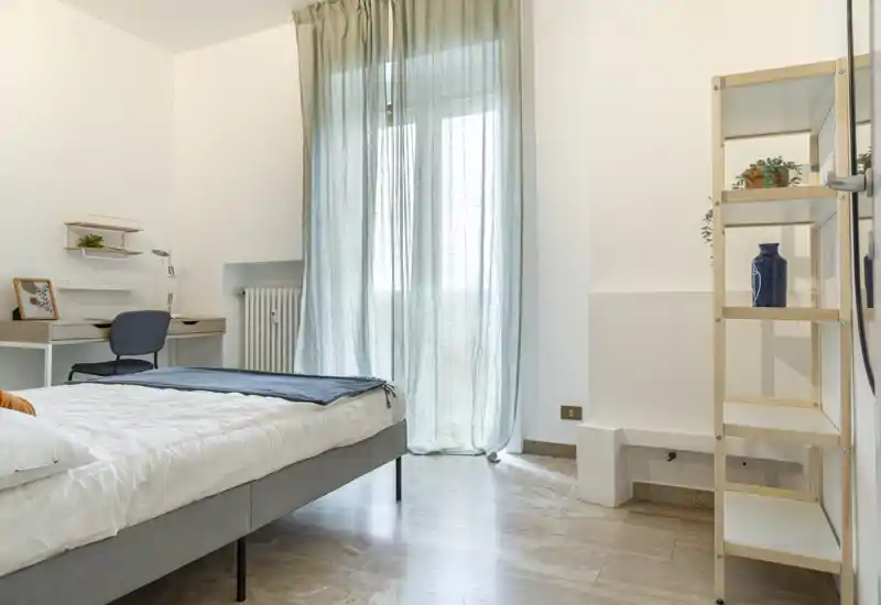 Bright, softly furnished bedroom with a double bed, sheer curtains and a small desk — calm minimalist styling and natural light.