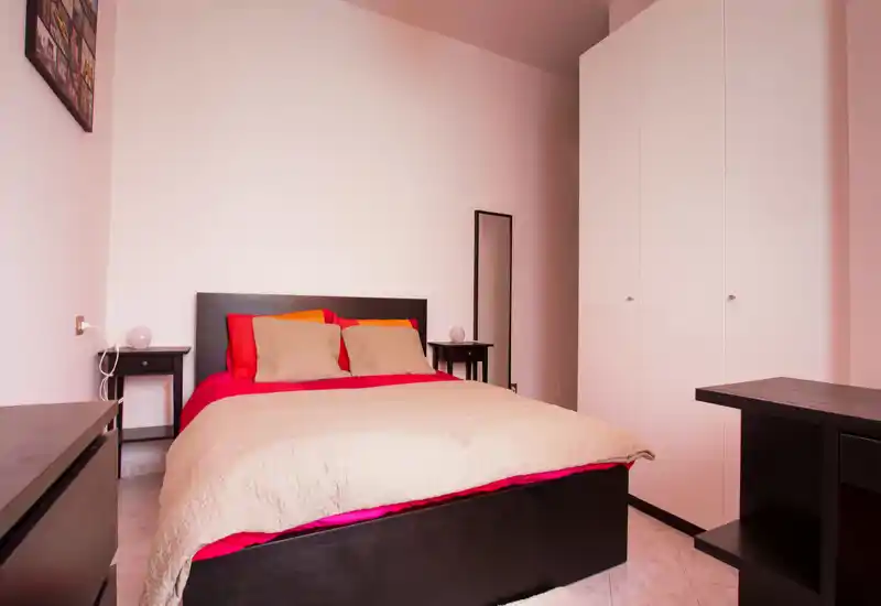 Bright, tidy bedroom with a large double bed, matching dark wood furniture and a white wardrobe; neutral decor and warm textiles create a welcoming atmosphere.