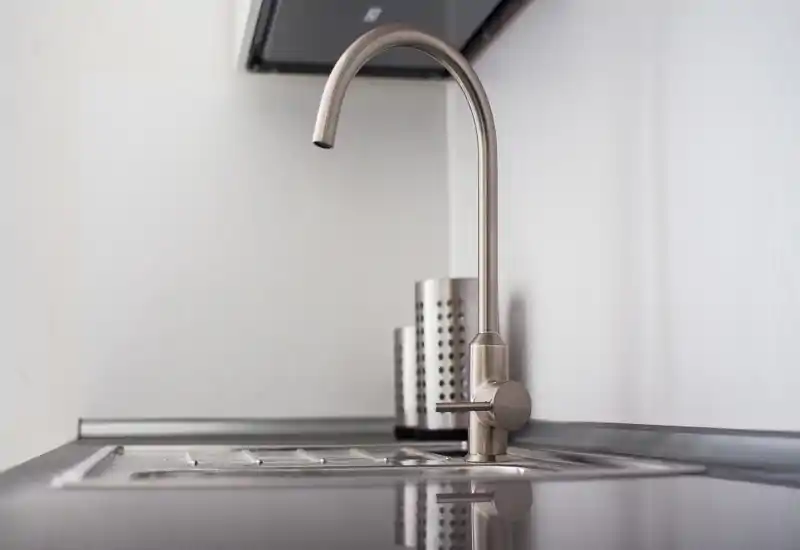 Primo piano di un lavello da cucina in acciaio inox con rubinetto curvo, piano pulito e portaposate minimal.