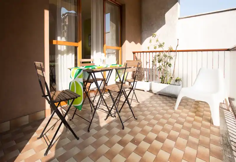 Balcone soleggiato arredato con tavolino pieghevole e sedie, pavimento piastrellato e fioriere — perfetto per la colazione o pasti leggeri.