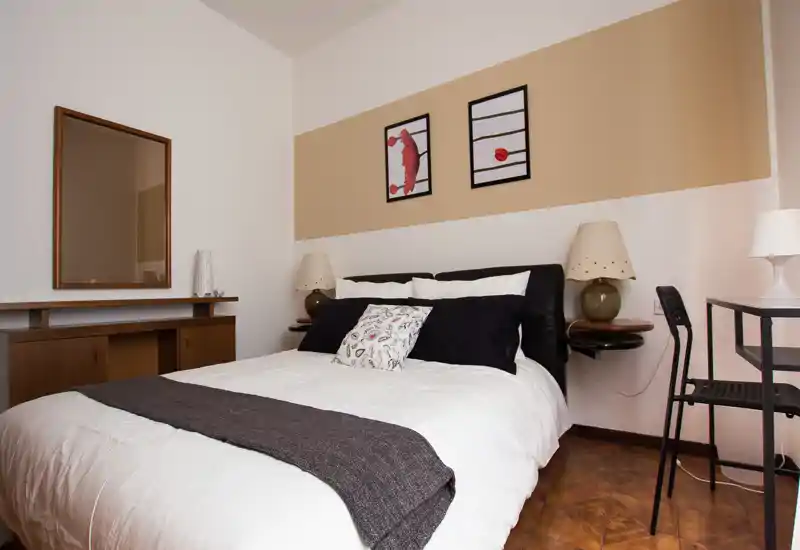 Camera da letto doppia luminosa e ben arredata con letto ordinato, lampade da comodino e quadri essenziali — accogliente e moderna.