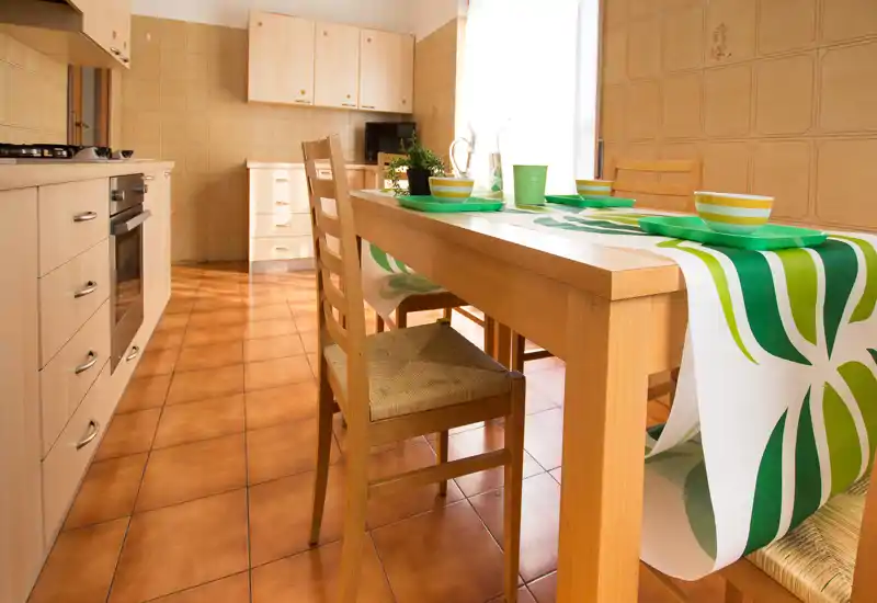 Cucina luminosa e ordinata con tavolo in legno apparecchiato per quattro e pavimento in cotto caldo — perfetta per i pasti in famiglia.