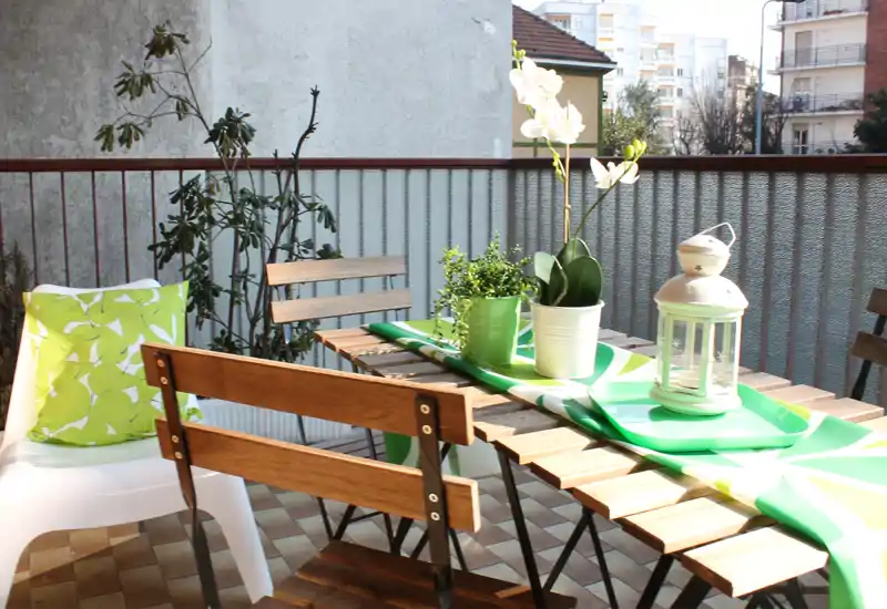 Balcone soleggiato arredato con tavolo e sedie in legno, piante decorative e una lanterna — ideale per colazioni o cene all'aperto.