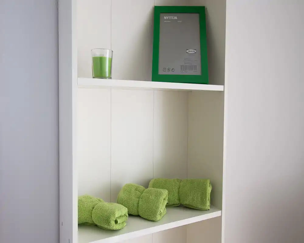 Close-up of a white built-in shelf with neatly folded green towels and a green-framed picture; a simple, fresh decorative vignette ideal for showing storage or styling details.