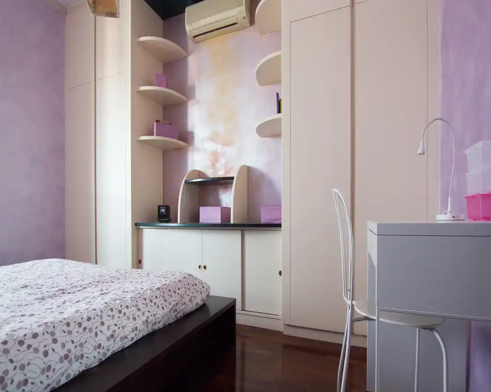 Bright, pastel bedroom with a low platform bed, built-in wardrobes and a small desk — calm, cozy atmosphere suitable for a single or guest room.