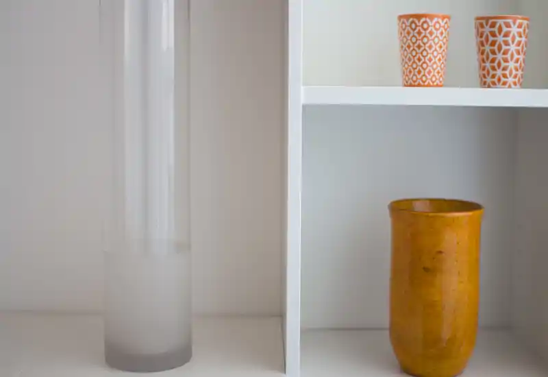 Primo piano di una mensola bianca con vasi e tazze decorative in ceramica. L'immagine mette a fuoco gli oggetti decorativi più che una stanza specifica.