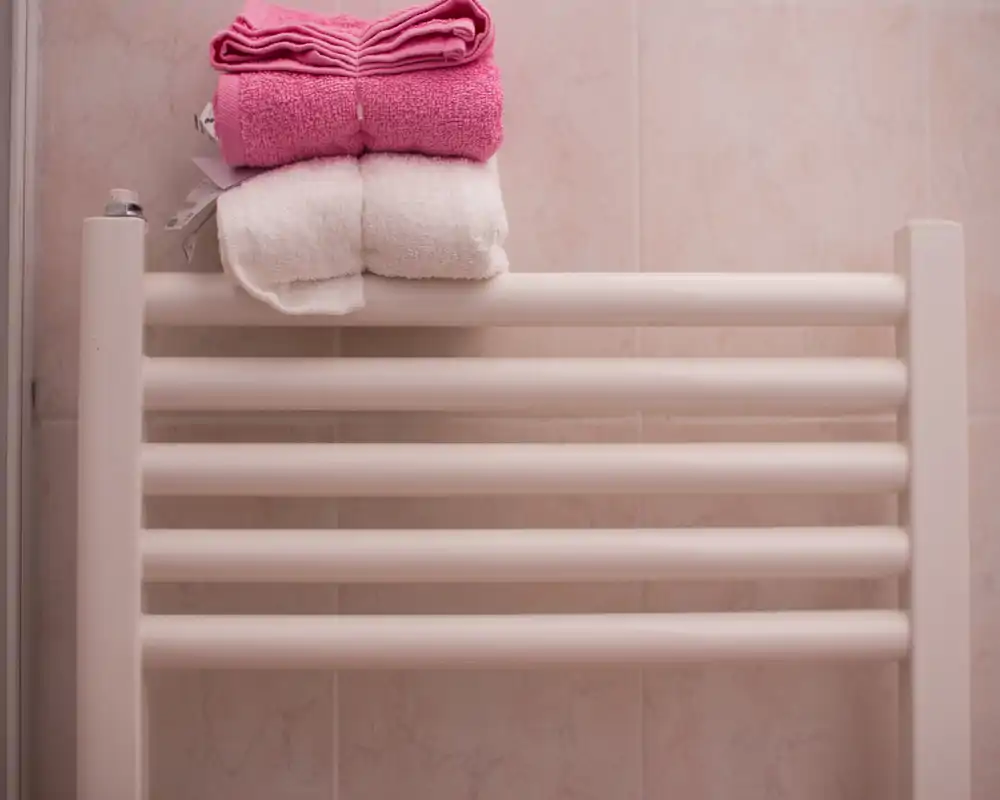 Primer plano de un toallero calefactado con toallas rosas y blancas dobladas, montado en la pared alicatada del baño.