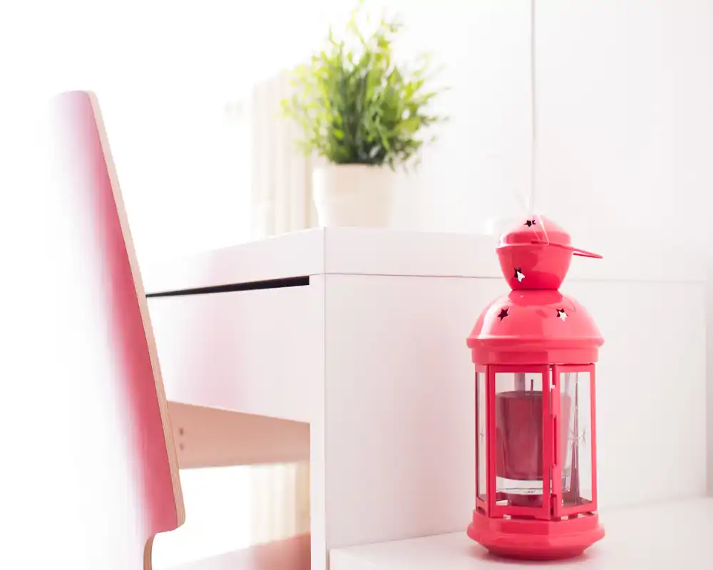 Foto luminosa y minimalista de un rincón con silla/escritorio, una linterna roja decorativa y una planta en maceta que aportan calidez.