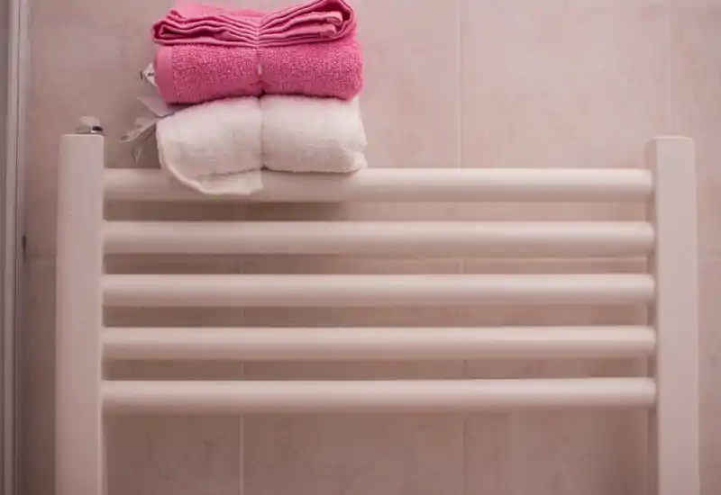 Gros plan d'un sèche-serviettes chauffant avec des serviettes roses et blanches pliées, fixé sur un mur carrelé de salle de bains.