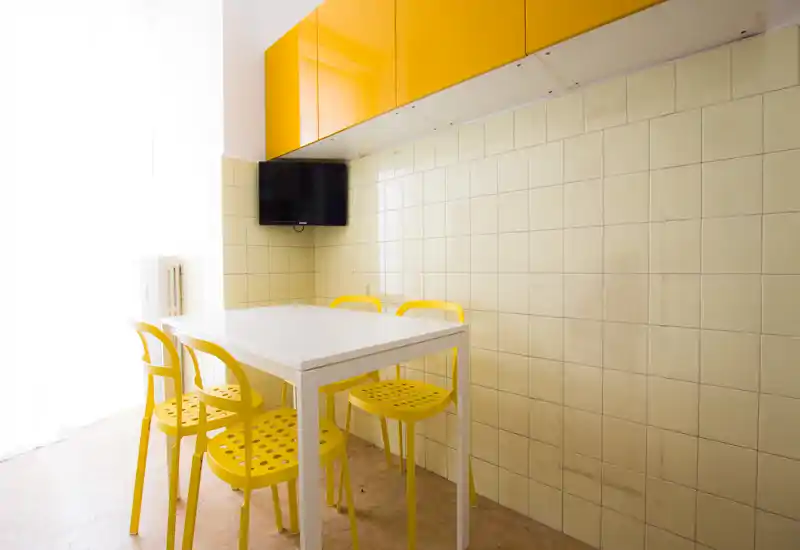 Coin cuisine compact et moderne avec table blanche et quatre chaises jaunes, placards jaunes brillants et crédence carrelée — un coin repas lumineux et gai.