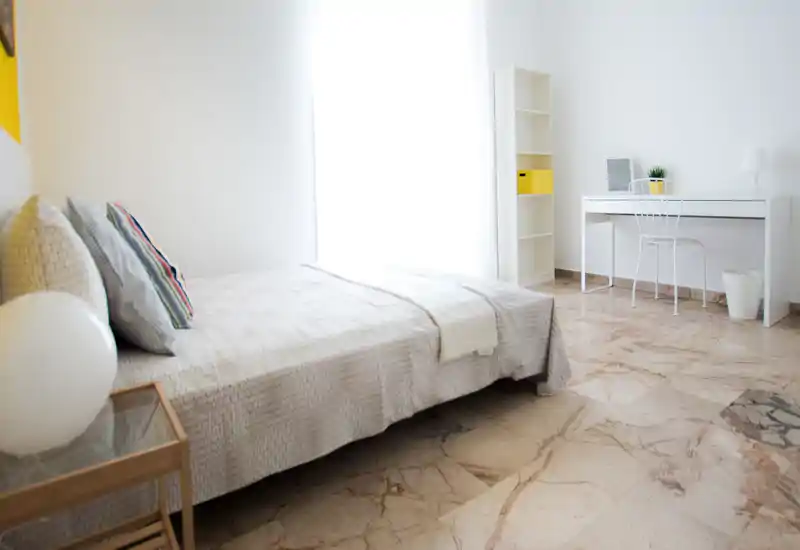 Dormitorio luminoso y minimalista con cama grande, ropa de cama suave y un pequeño escritorio junto a la ventana — ideal para descansar y trabajar en remoto.