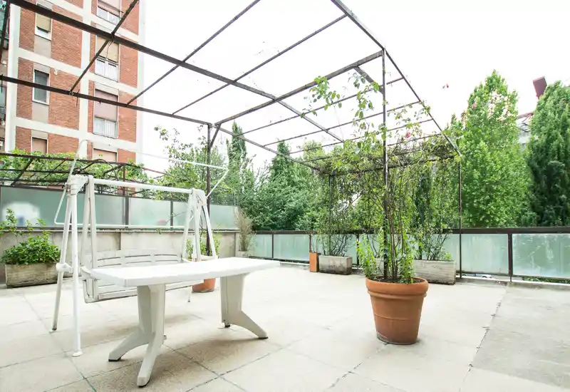 Bright private terrace with potted plants, a pergola frame and a white outdoor bench/swing — ideal for relaxation and small gatherings.