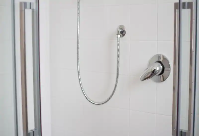 Close-up of a modern shower with chrome fixtures and white tiled walls — clean and well-lit bathroom detail.