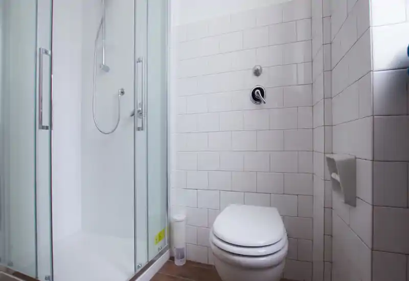 Bright, modern bathroom with a glass shower enclosure and wall-mounted toilet, white subway tiles and wood-effect floor.