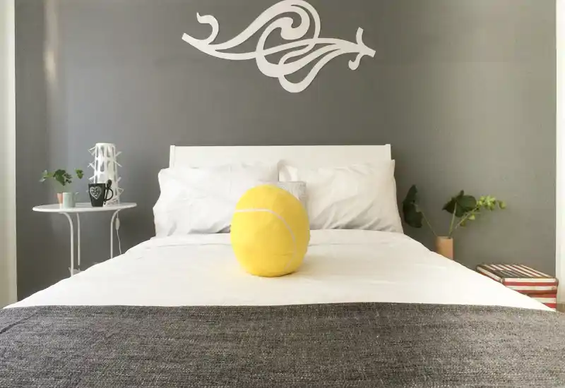 Dormitorio luminoso y moderno con cama bien hecha, cojines decorativos y mesitas sencillas — ambiente minimalista y relajante, ideal para el anuncio.