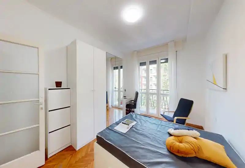Dormitorio moderno y luminoso con cama cómoda, grandes ventanas y un pequeño espacio de trabajo junto al balcón — ideal para quienes valoran la luz natural y el diseño minimalista.