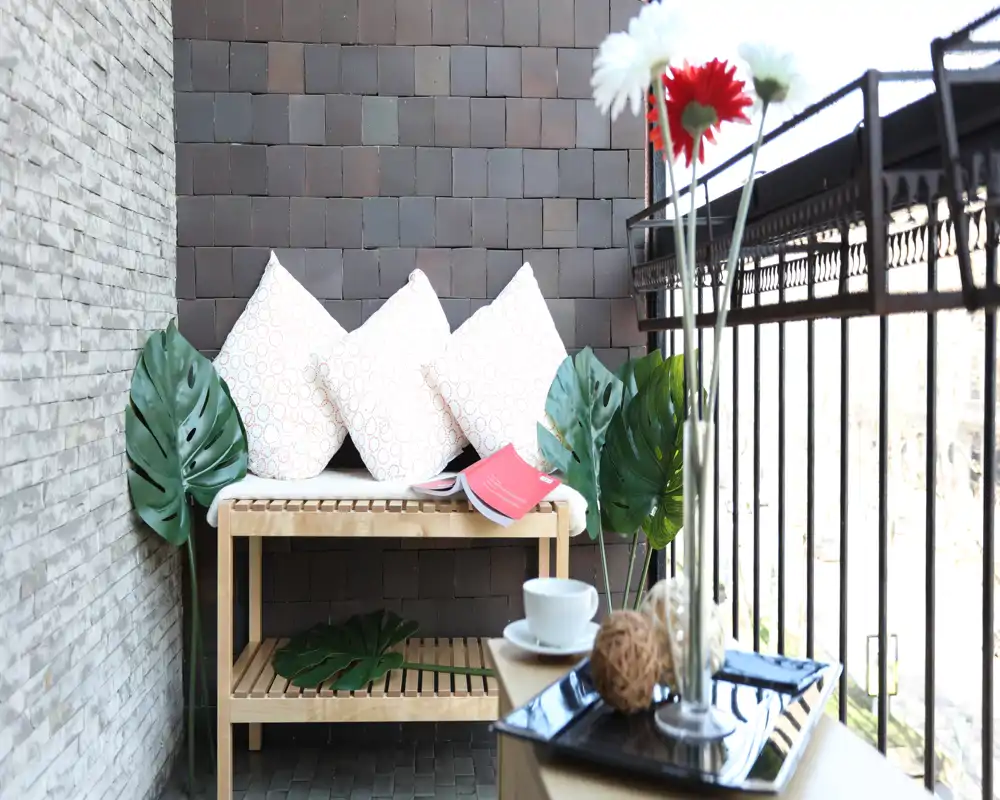 Acogedor rincón en el balcón con banco de madera, cojines decorativos y plantas — un lugar luminoso e ideal para el café matutino.
