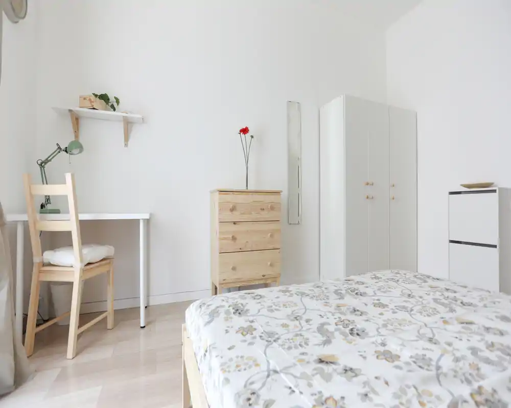 Dormitorio luminoso y minimalista con colcha estampada, muebles de madera y un pequeño escritorio — ideal para alquileres de corta estancia que buscan habitaciones limpias y espaciosas.