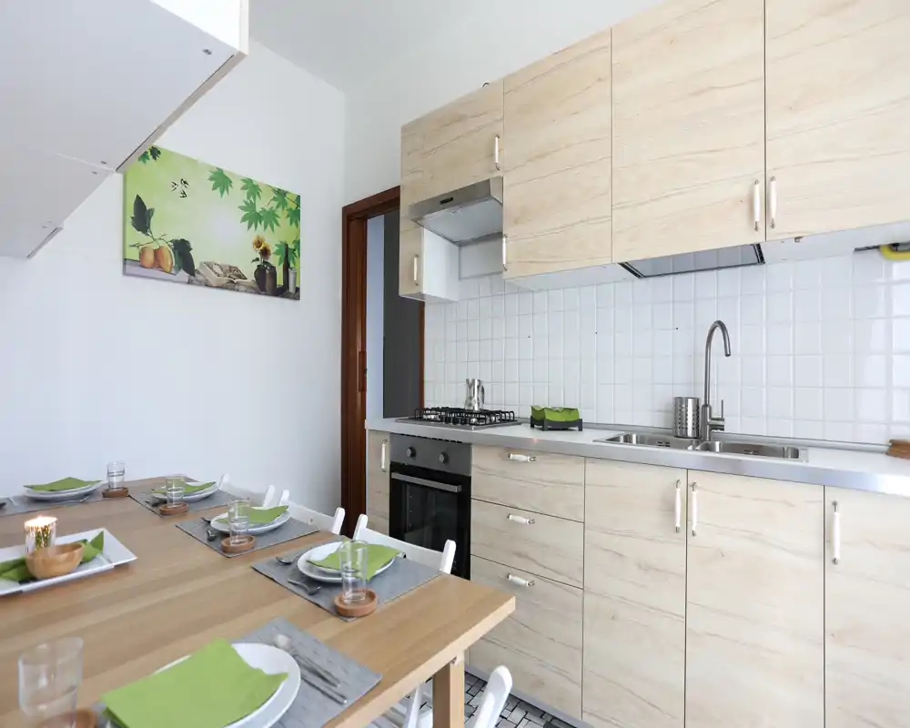 Cocina moderna y luminosa con muebles de madera clara, fregadero y cocina de acero inoxidable y una mesa de comedor de madera puesta para cuatro — espacio limpio y acogedor.