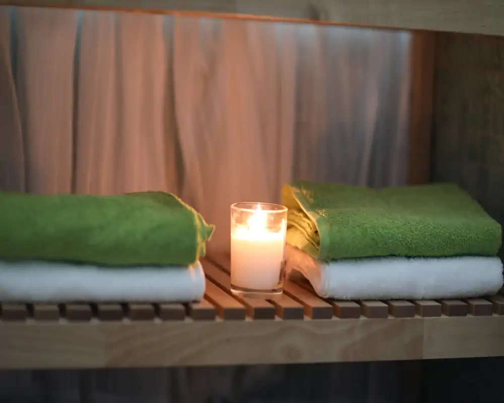 Toallas dobladas ordenadamente en una estantería de madera con una vela encendida, que sugiere un rincón de baño relajante tipo spa.