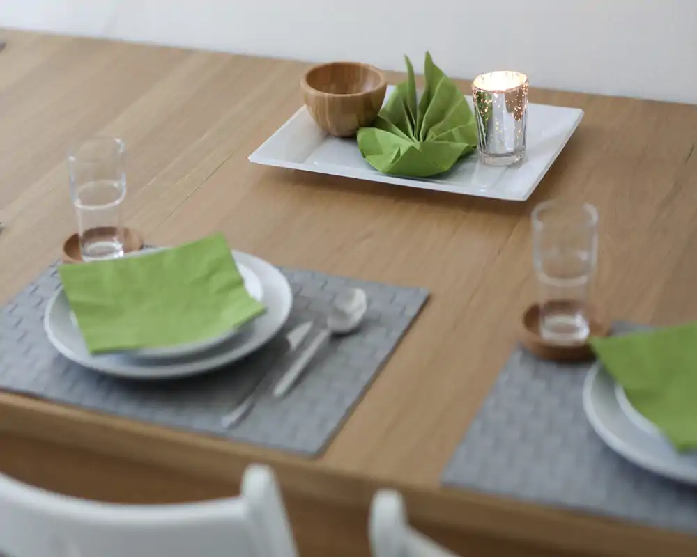 Mesa de comedor elegante puesta con servilletas verdes, cristalería y una vela decorativa que crea un ambiente acogedor para las comidas.