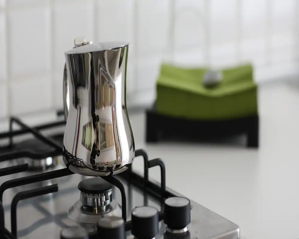 Primer plano de una vitrocerámica de gas con una cafetera metálica pulida en foco; cocina moderna, luminosa y de estilo minimalista con fondo desenfocado.