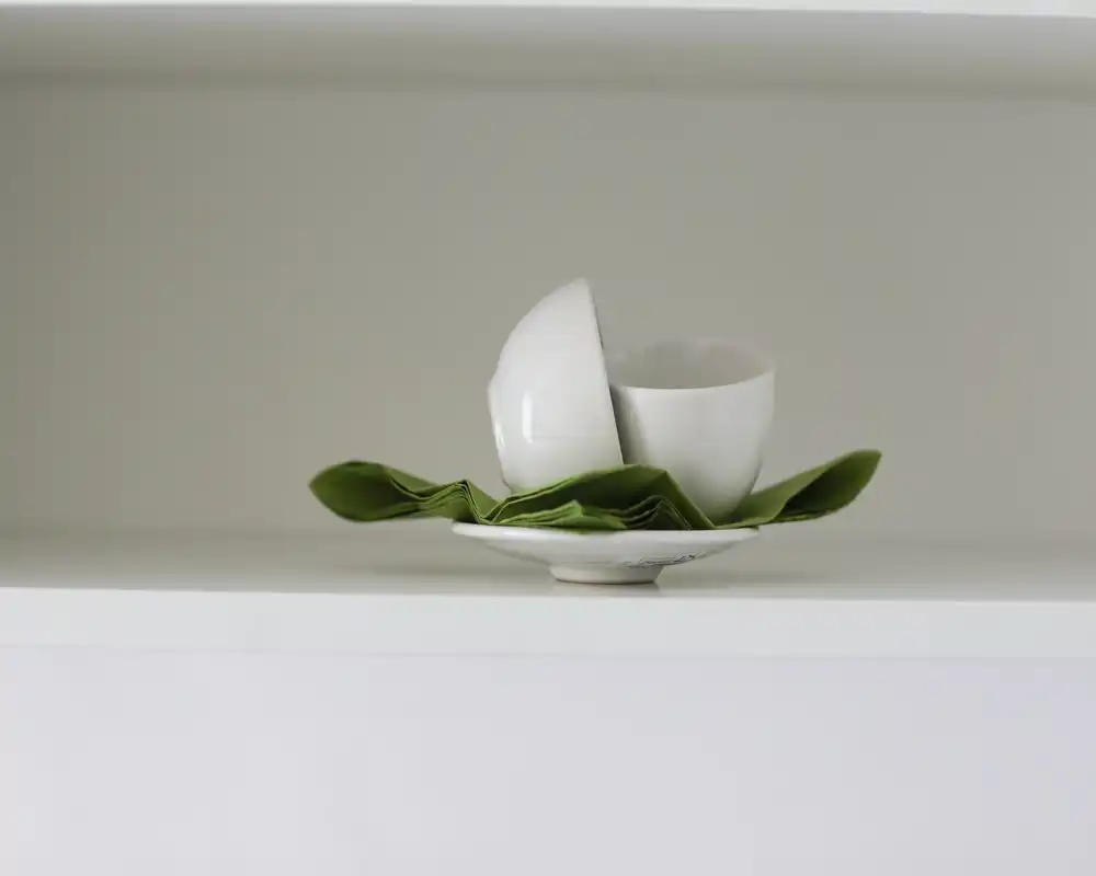 Primer plano de cuencos/tazas blancas en un estante con una servilleta verde; contexto mínimo y sin elementos que permitan identificar la habitación.