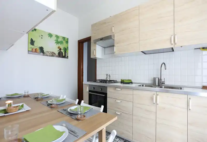 Cuisine moderne et lumineuse avec placards en bois clair, évier et cuisinière en acier inoxydable, et une table en bois dressée pour quatre — espace propre et accueillant.