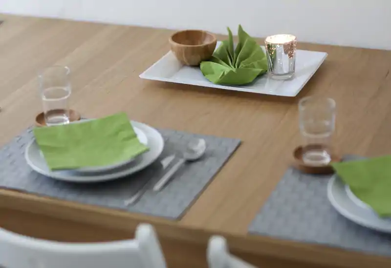 Table à manger élégante dressée avec serviettes vertes, verrerie et une bougie décorative créant une ambiance chaleureuse.