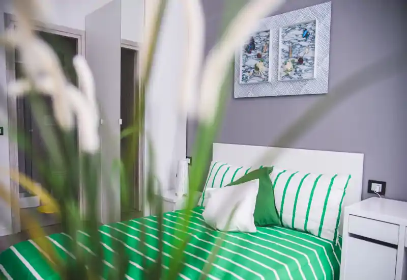 Bright, modern bedroom with a white headboard and green-striped bedding; decorative pillows and framed art create a fresh, inviting look.