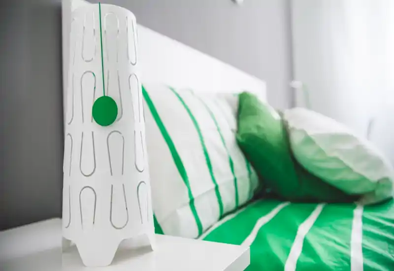 Close-up bedroom shot showing a striped green-and-white bed with pillows and a modern bedside lamp; bright, crisply styled and welcoming.